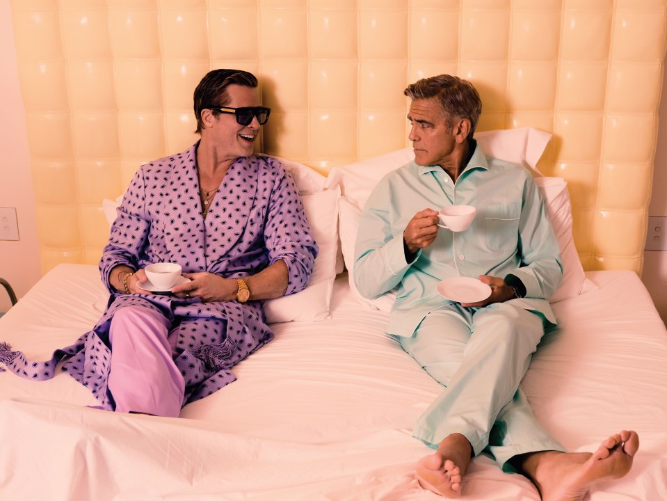 two men in pajamas are sitting on a bed drinking coffee