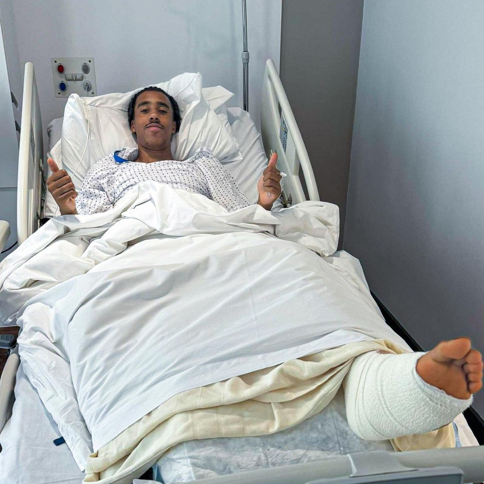 a man in a hospital bed with a broken leg gives a thumbs up