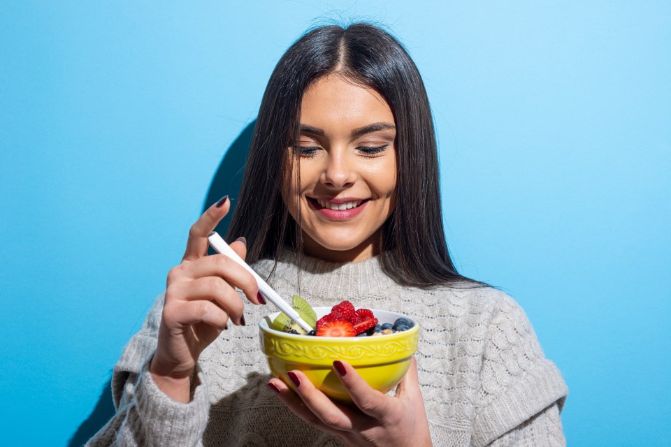 a woman is eating a bowl of fruit with a spoon