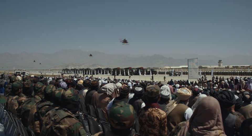 a crowd of people watching a helicopter fly overhead