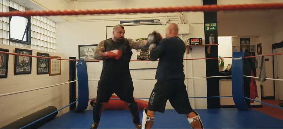 two men boxing in a ring with a fire exit sign above them