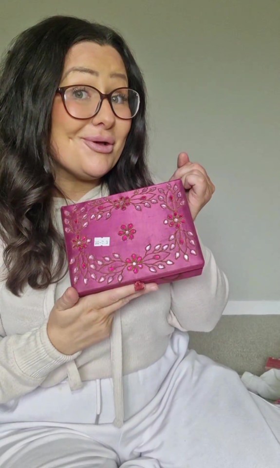 a woman wearing glasses is holding a pink box with flowers on it