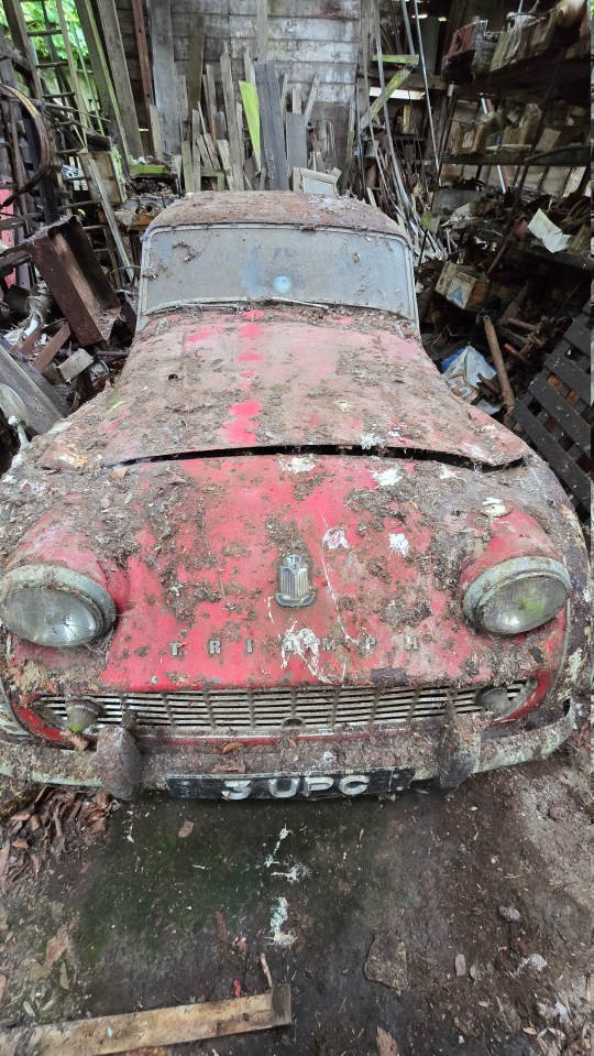 a red triumph car sits in a messy garage