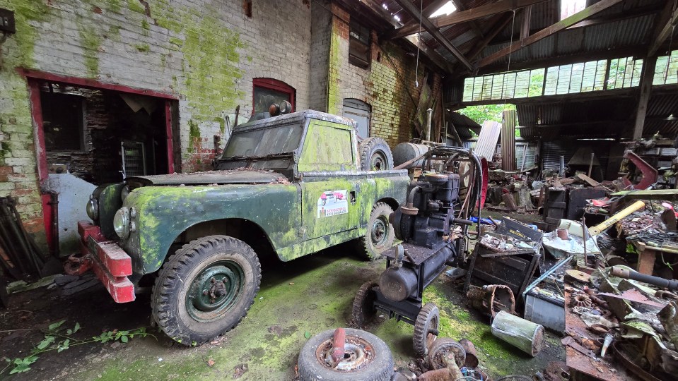 a green land rover is parked in a messy garage