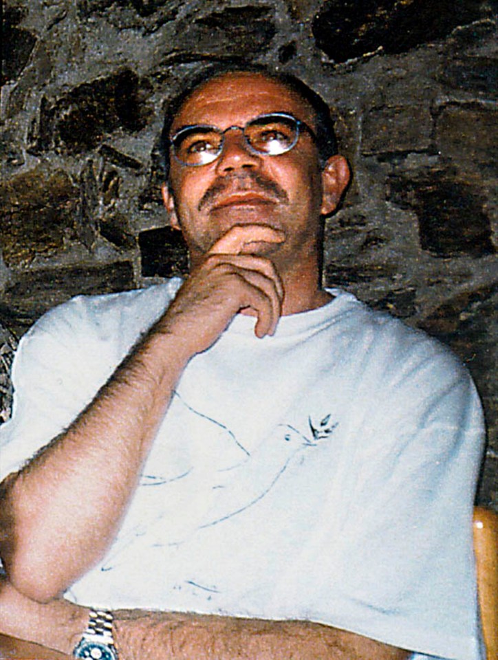 a man wearing glasses and a watch sits in front of a stone wall