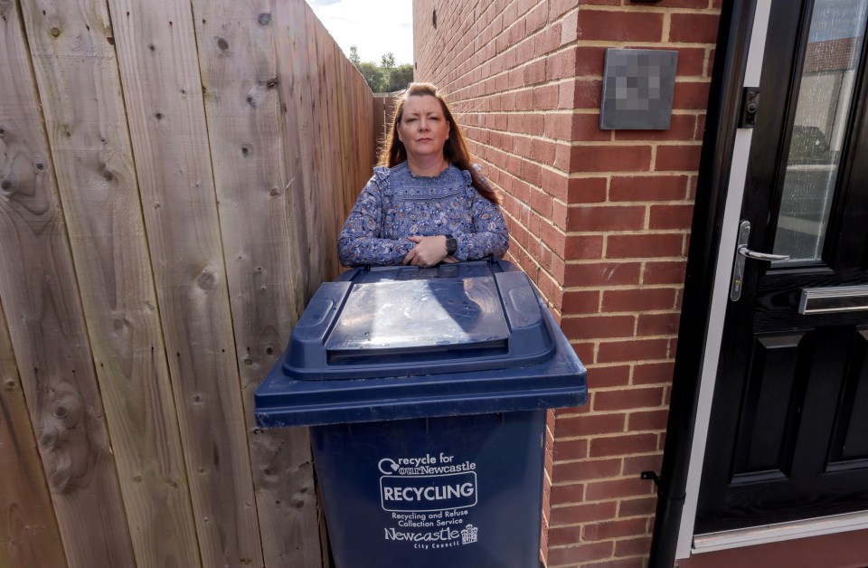 a woman stands next to a blue recycling bin