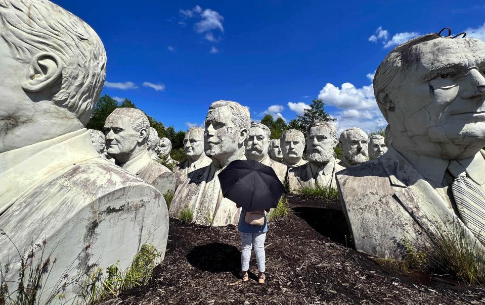 a woman holding an umbrella stands in front of a row of statues