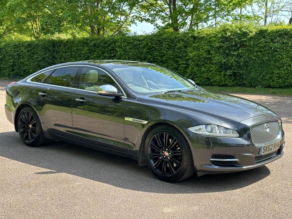 a gray jaguar is parked in front of a hedge