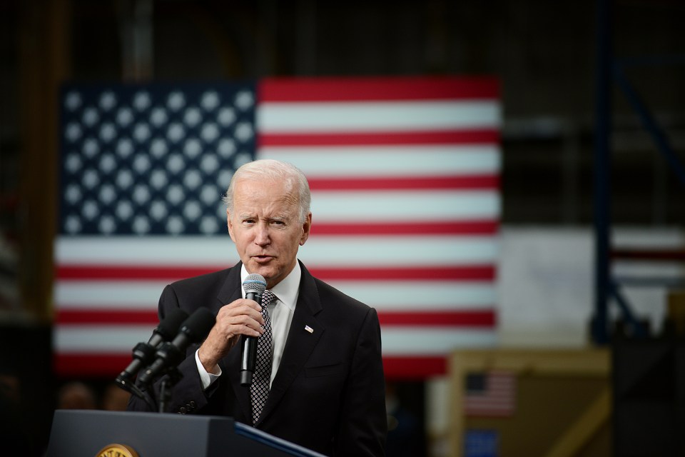 a man speaking into a microphone with an american flag in the background