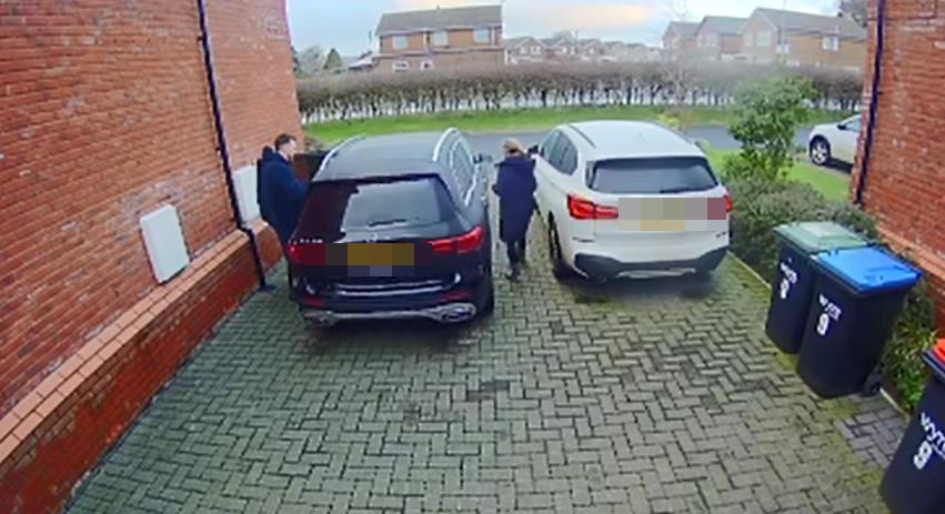 a couple of people standing next to a car in a driveway .