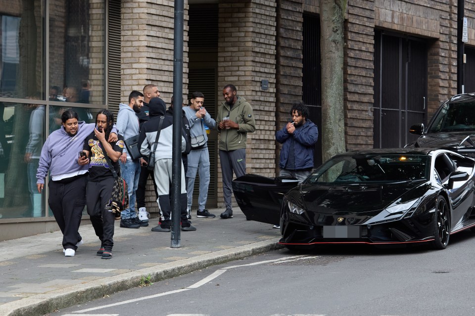 a group of people are standing on a sidewalk in front of a building with a black car parked in front of it