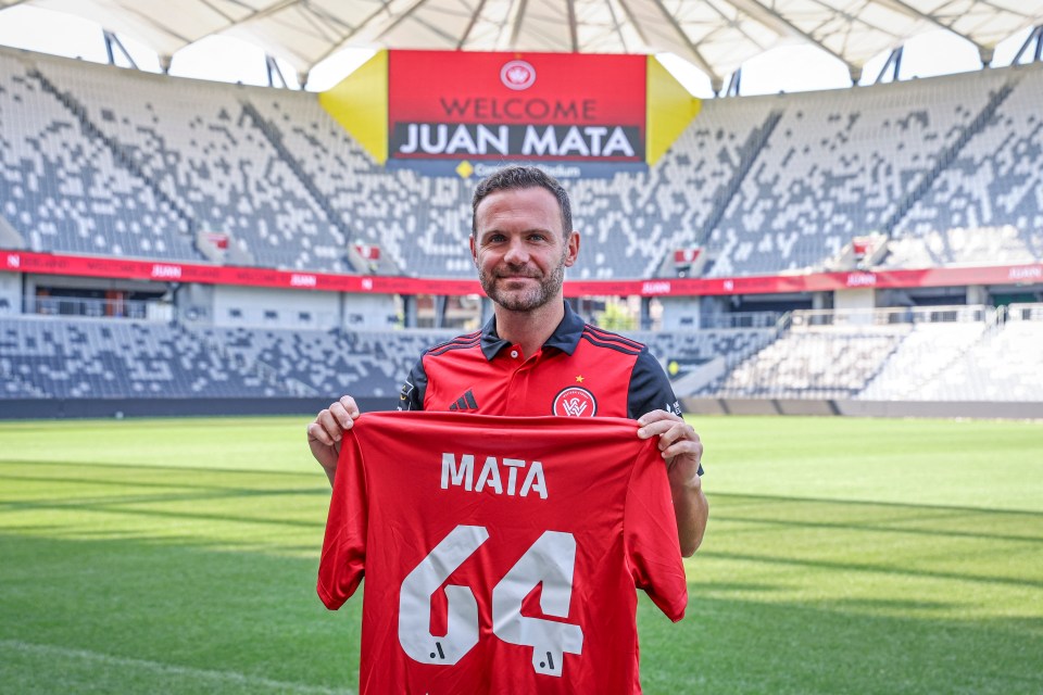 a man holds up a red jersey with the name mata on it