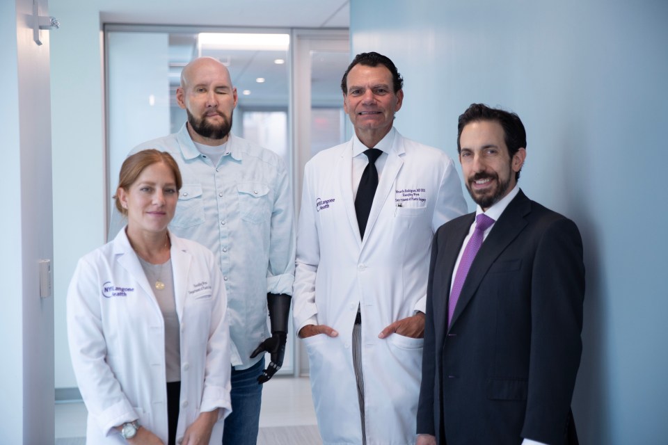 a man with a prosthetic arm stands between two doctors and a man in a suit