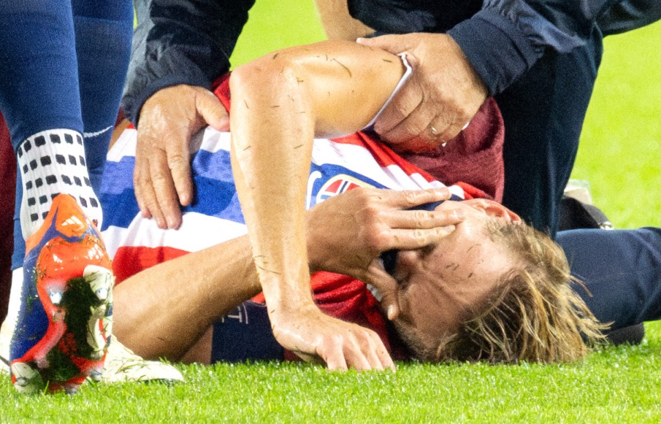 a soccer player is laying on the field with his head in his hands