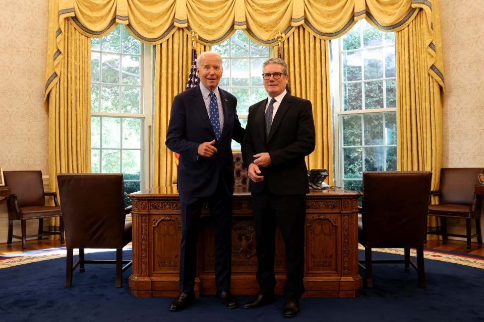 two men are standing in front of a desk in a room