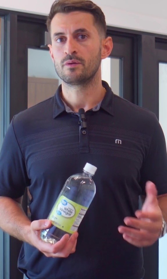 a man in a black shirt is holding a bottle of white vinegar