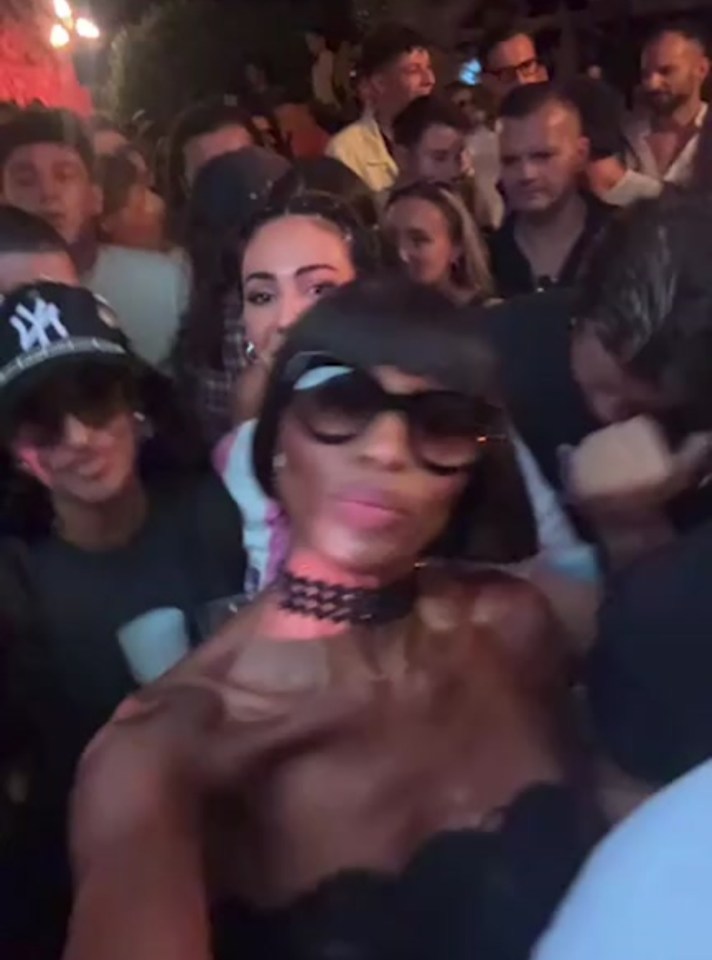 a woman wearing sunglasses and a choker stands in a crowd of people .