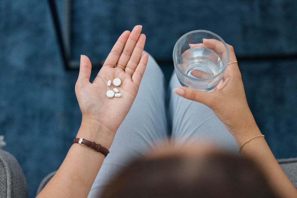 a woman is holding a glass of water and a handful of pills