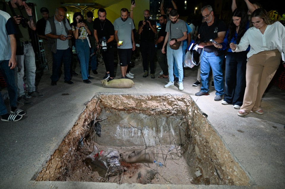 People stand over a crater after Lebanese army soldiers blew up one device