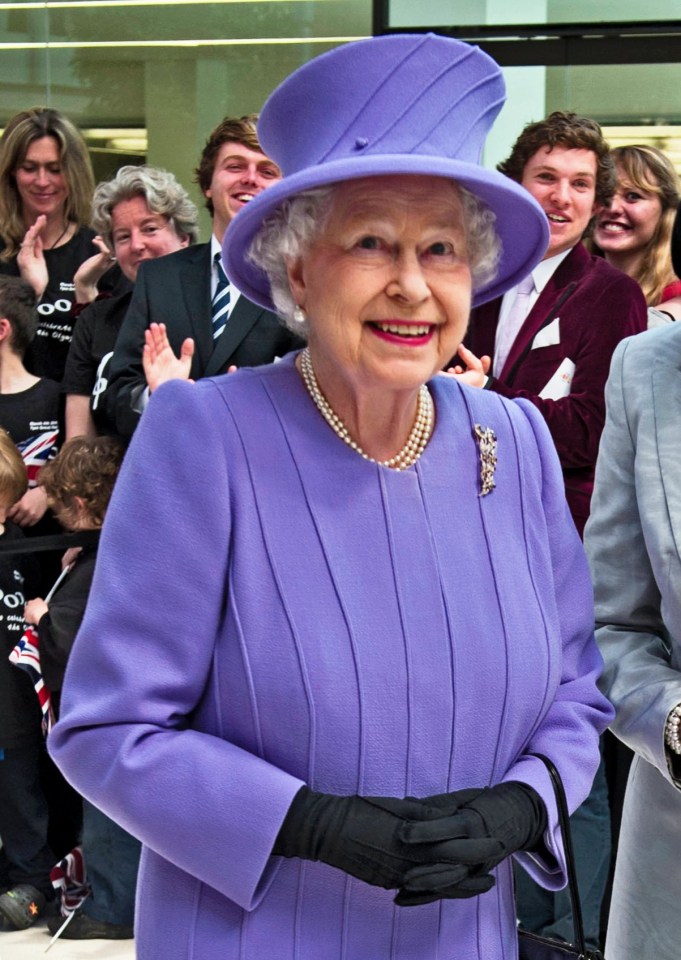 queen elizabeth ii wearing a purple dress stands next to a woman