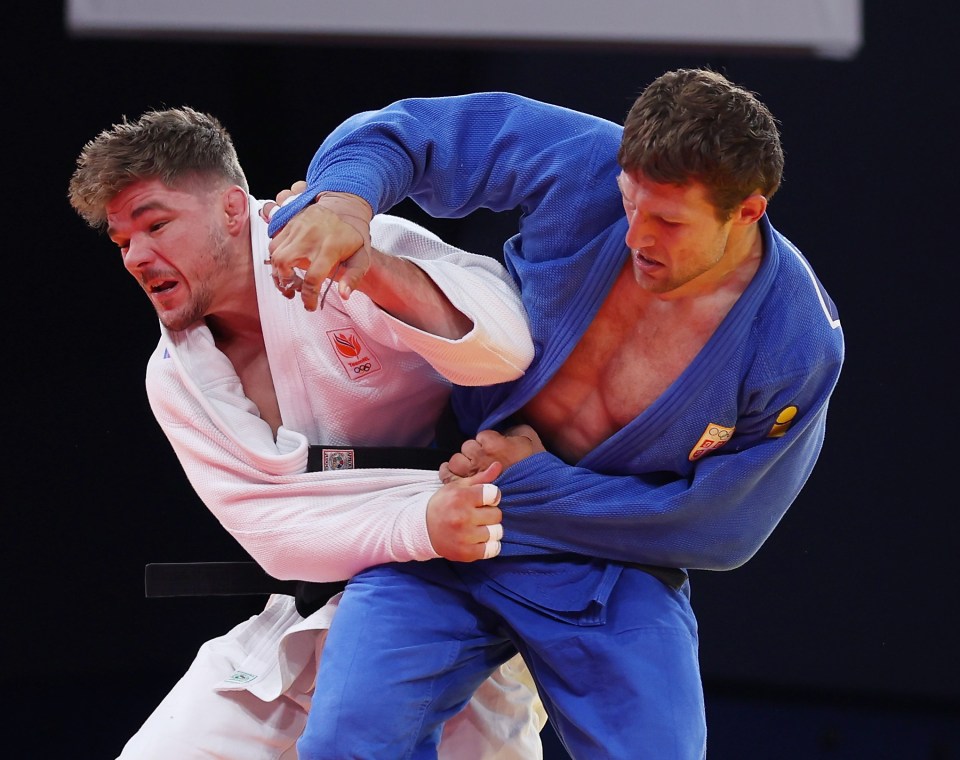 two judo fighters are wrestling in front of an olympic flag