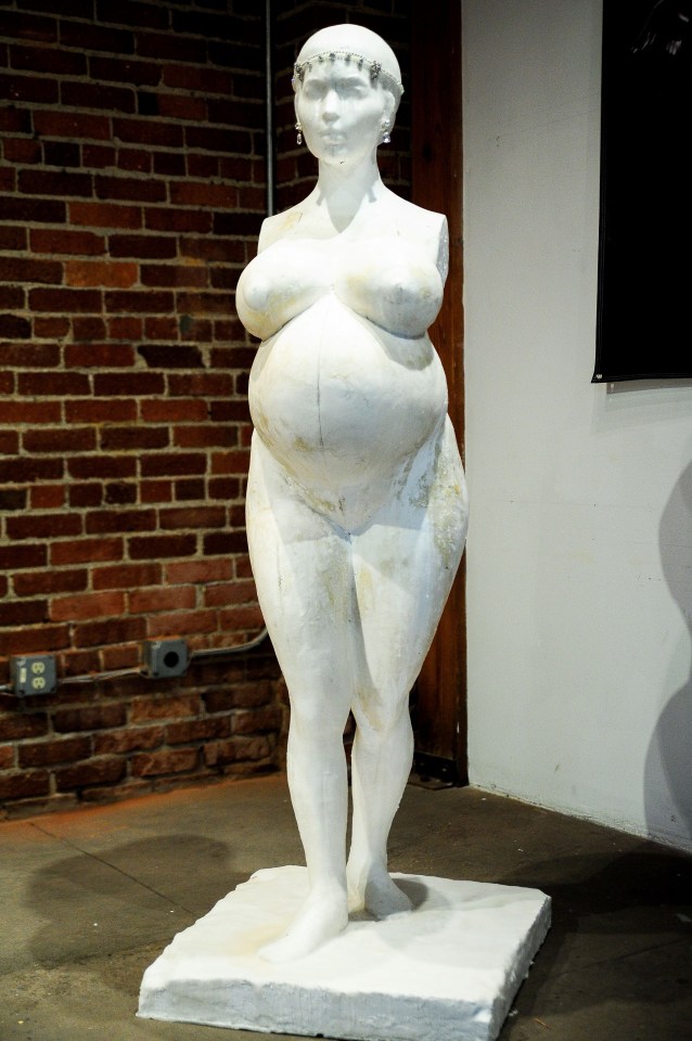 a statue of a woman with a large belly is in front of a brick wall