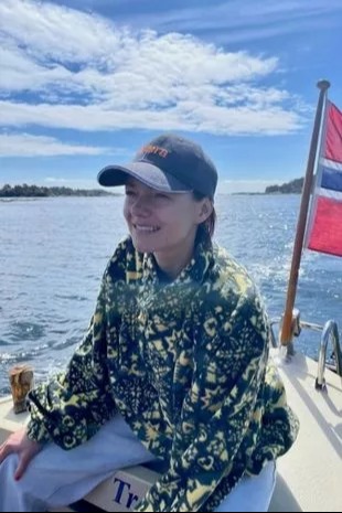 a woman is sitting on a boat in the water wearing a hat and a jacket .