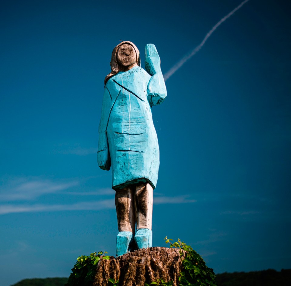 a statue of a woman in a blue coat stands on top of a tree stump