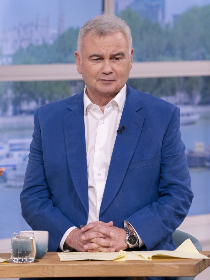 a man in a blue suit sits at a table with his hands folded