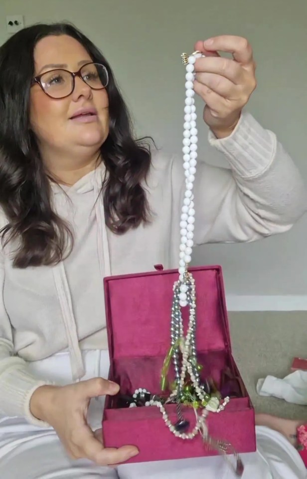 a woman is holding a necklace in a pink box