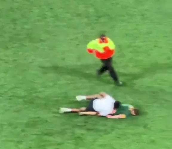 a man is laying on the ground on a soccer field while a referee runs towards him .