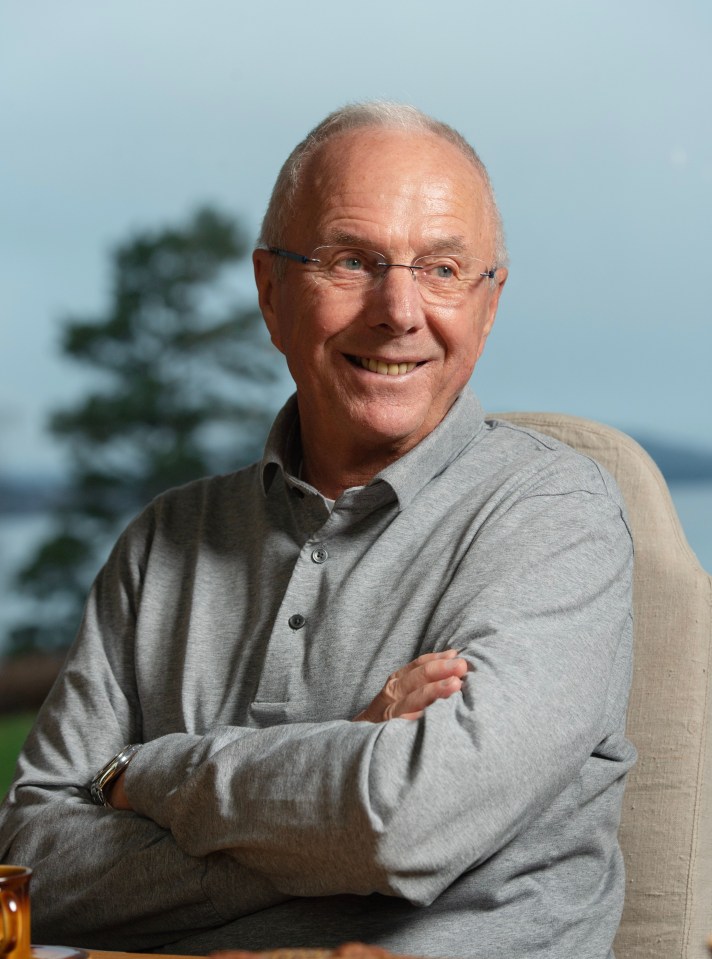 a man in a grey shirt and glasses is smiling with his arms crossed