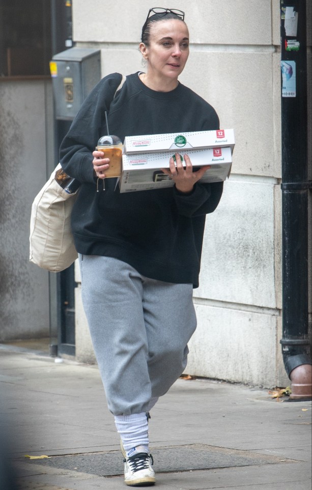 a woman is carrying a box of pizza and a cup of coffee