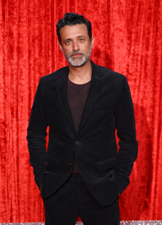 a man in a black suit stands in front of a red curtain