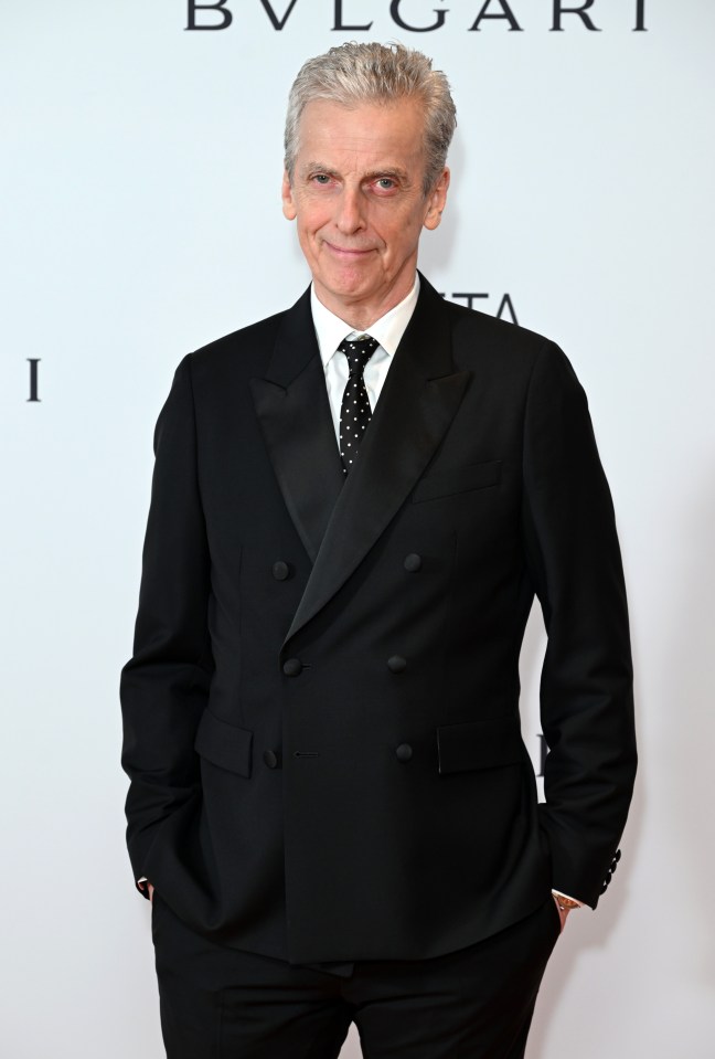 a man in a tuxedo stands in front of a bvlgari sign