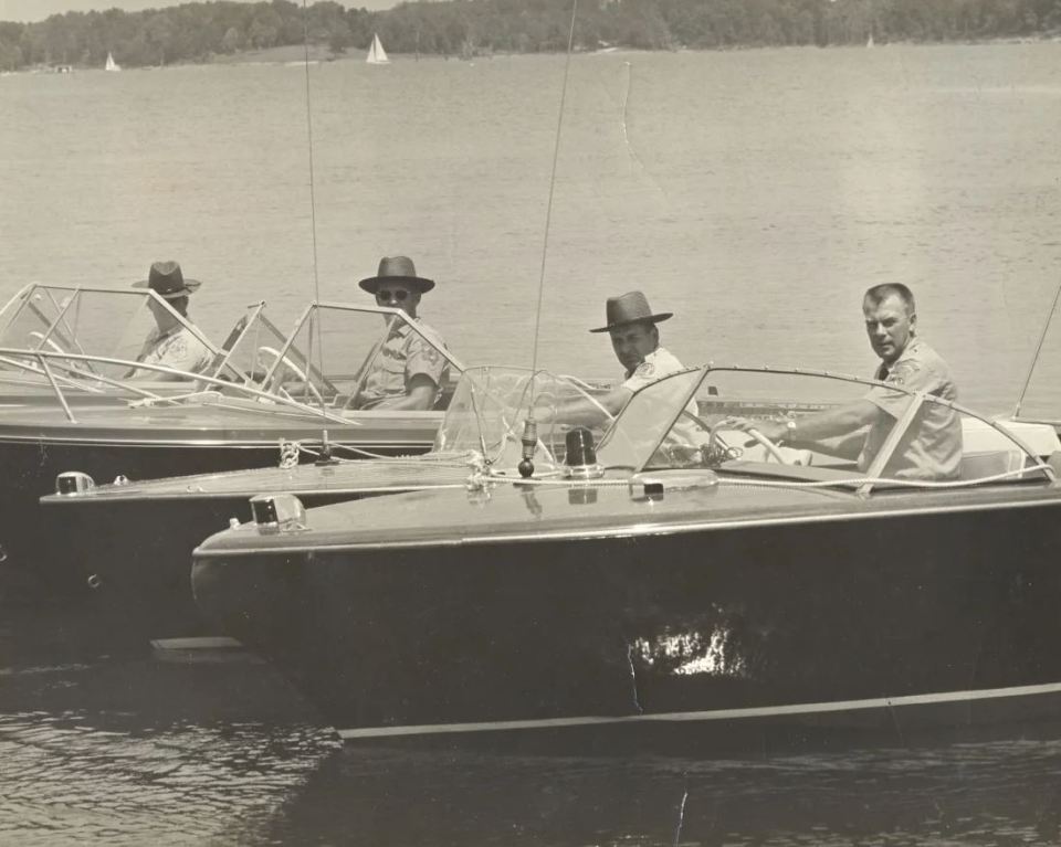 a black and white photo of three men in boats on a lake