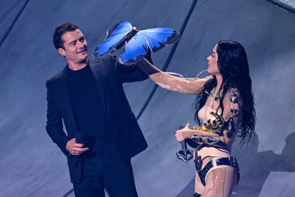 a man in a suit holds a blue butterfly while a woman in a bodysuit holds scissors