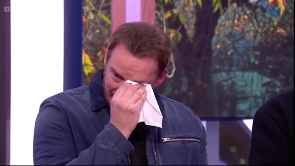 a man in a blue jacket wipes his eyes with a napkin