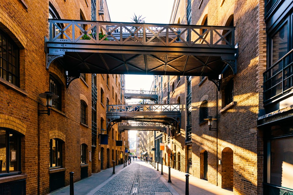 a bridge over a cobblestone street between two brick buildings