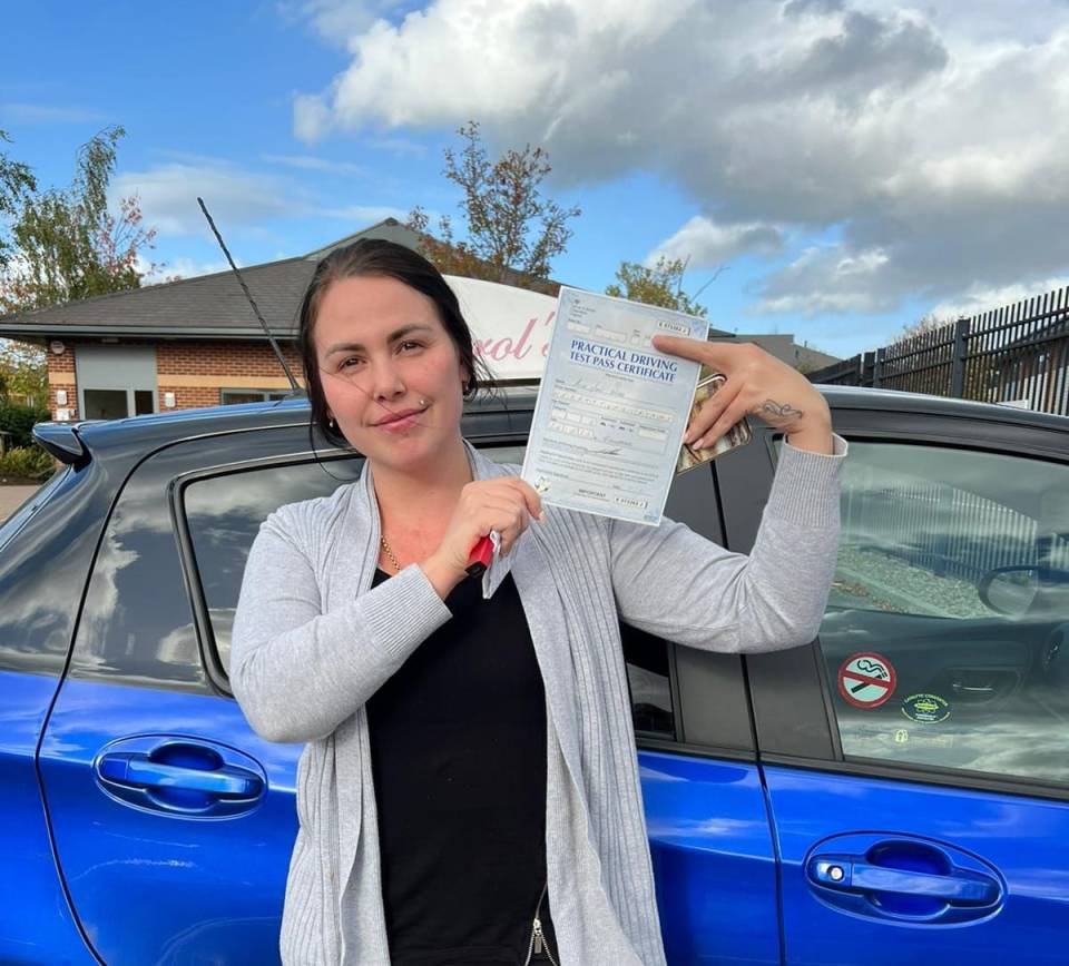 a woman holding a practical driving test certificate in front of a blue car