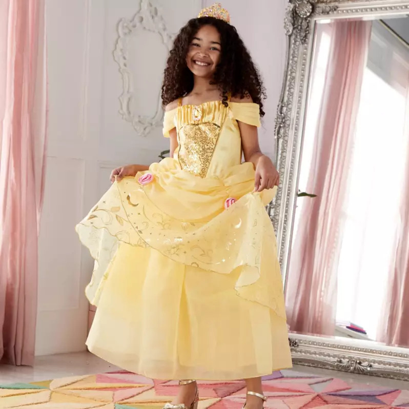 a little girl in a yellow princess dress is standing in front of a mirror