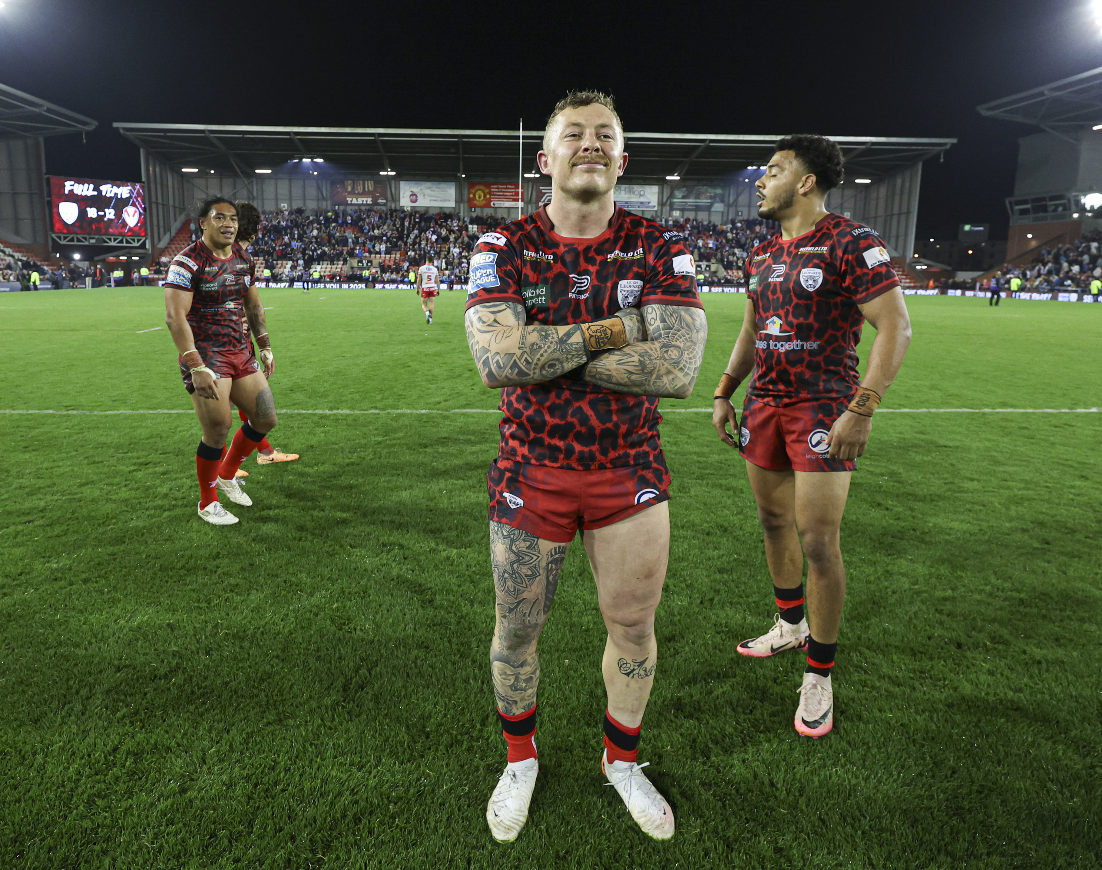 a rugby player stands on the field with his arms crossed