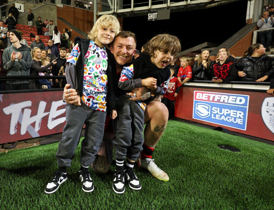 a man and two children pose for a photo in front of a betfred super league sign