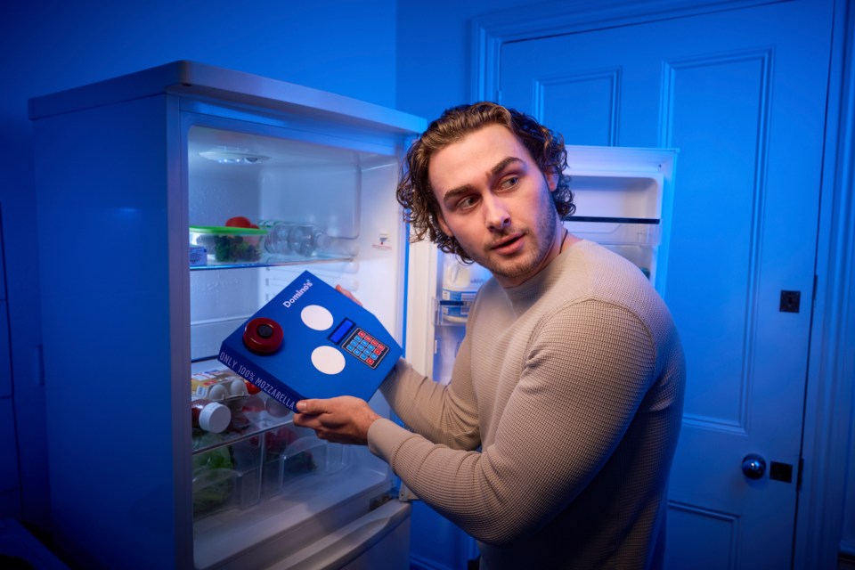 a man holding a box of domino 's pizza in front of an open refrigerator