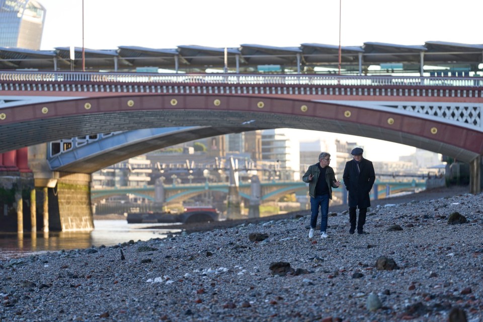 two men walking under a bridge with a building in the background that says ' tower bridge '