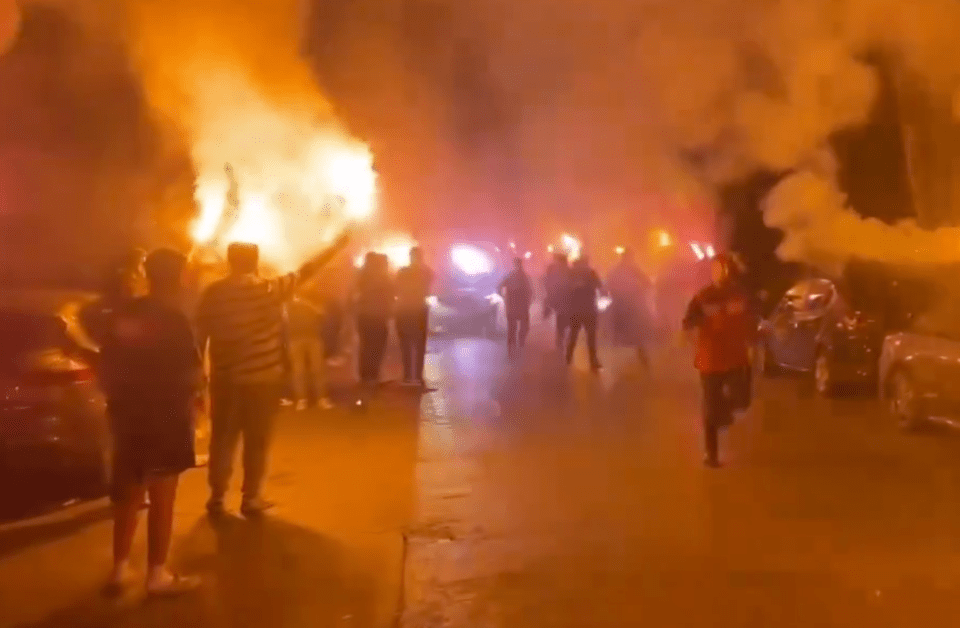 a group of people standing in front of a fire with smoke coming out of it