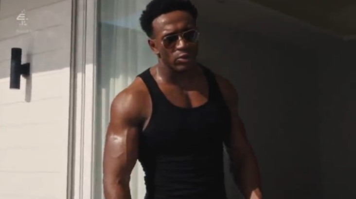 a man wearing sunglasses and a black tank top is standing in front of a window .