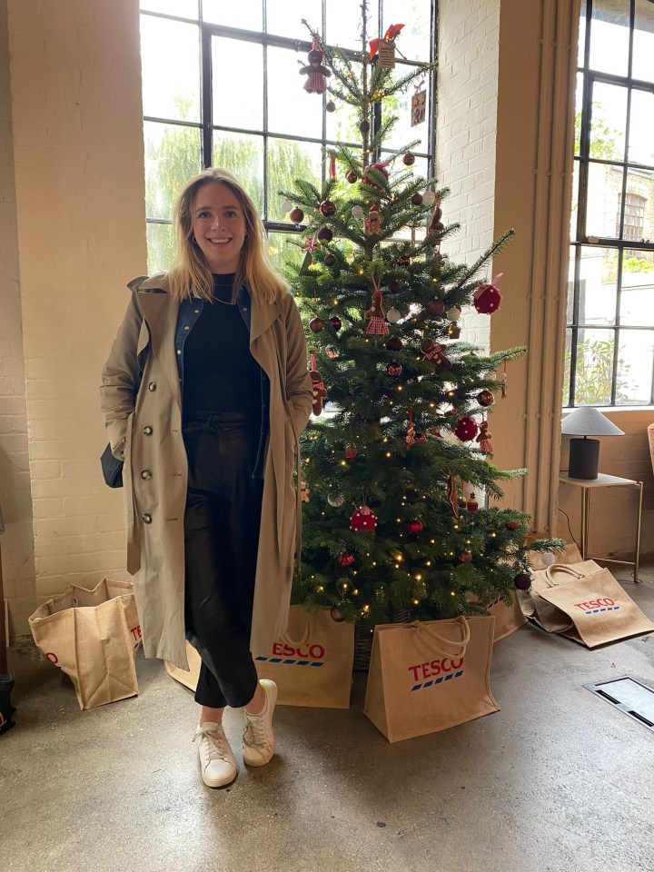 a woman stands in front of a tesco christmas tree