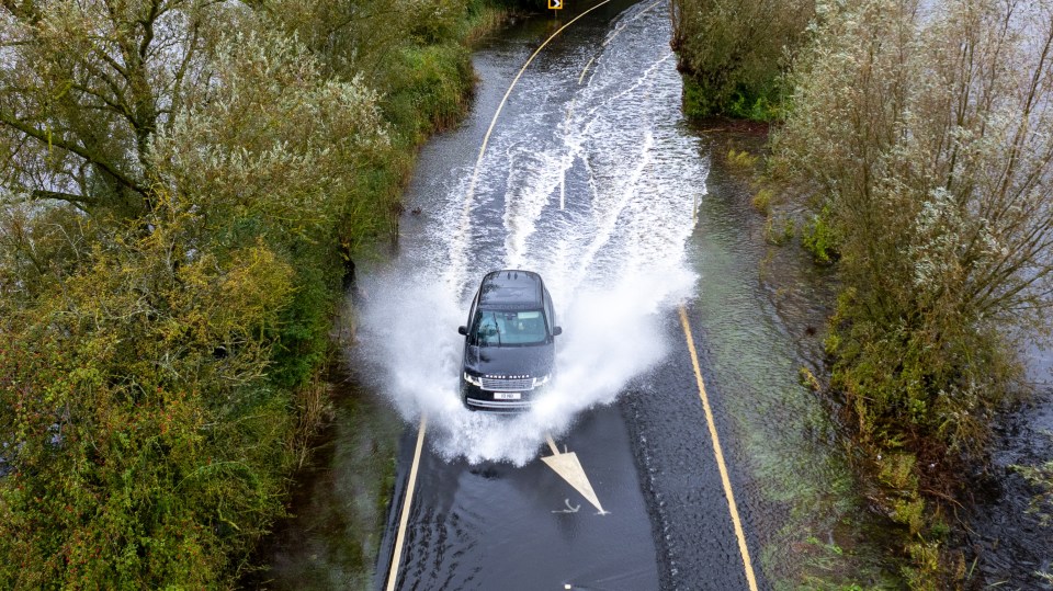 a black range rover is driving through a flooded road