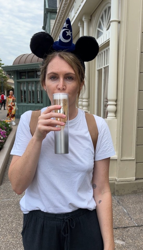 a woman wearing mickey mouse ears is drinking from a stainless steel cup